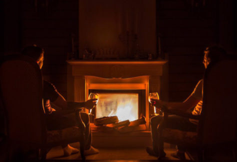 Zwei Personen sitzen vor Kamin mit Getränk
